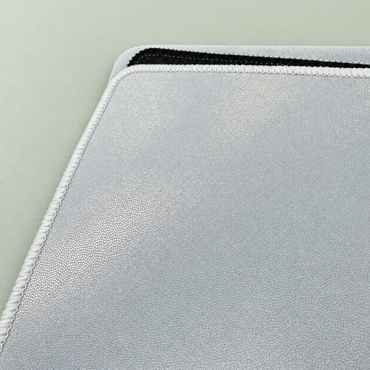 Close-up of holofoil playmat rounded corner with white stitched edge and sparkling pearlescent surface