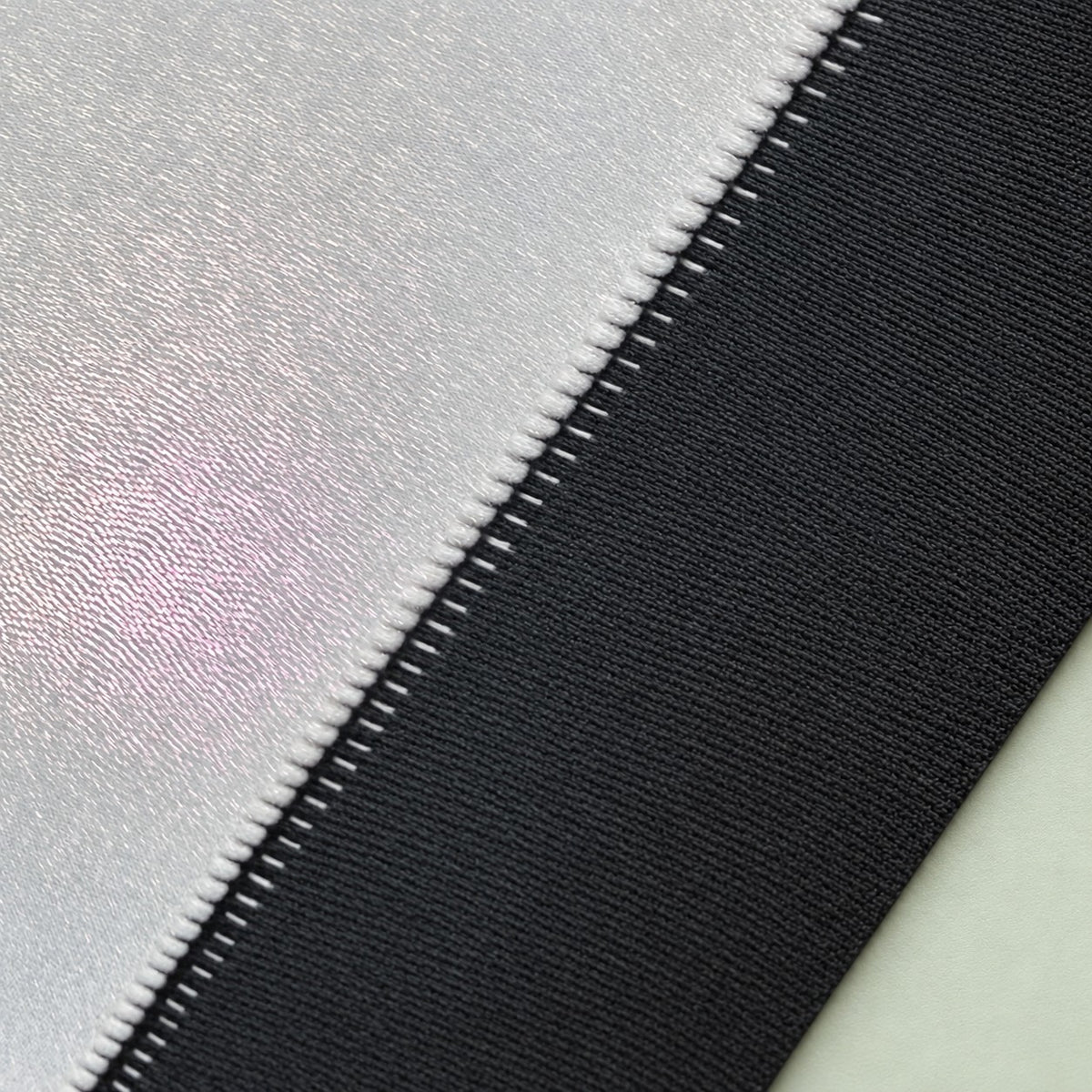 Macro close-up of white edge stitching between the holographic surface and black rubber base of a sublimation playmat